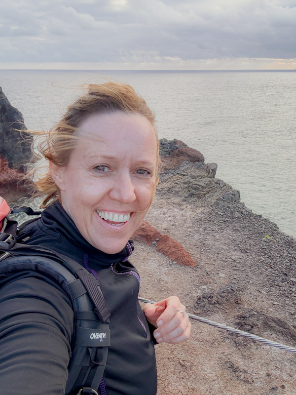 Nicola Lederer lachend mit Kamerarucksack auf dem Rücken vor der Küste Madeiras