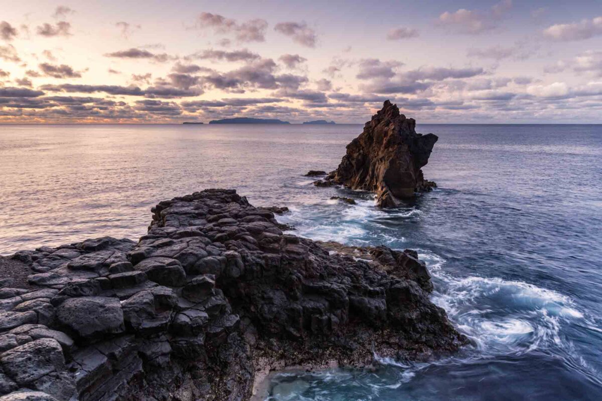 Vulkanfelsen an der Küste Madeiras bei Sonnenaufgang, mit einer markanten Felsnadel im Meer und weich fließendem Wasser um die Steine – ein Beispiel für Bildgestaltung mit führenden Linien und bewusster Motivplatzierung.